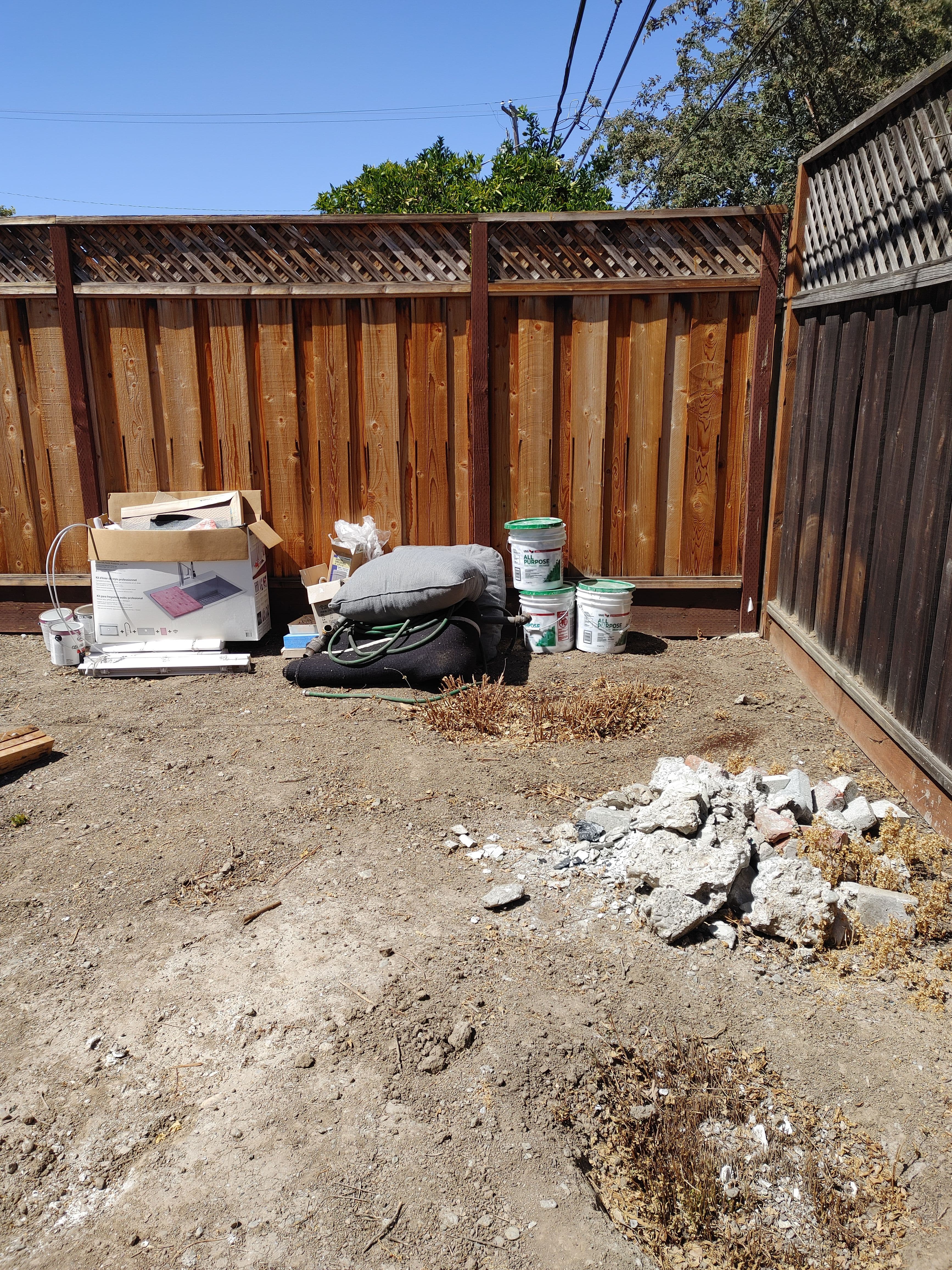 Construction site with debris, tools, and paint buckets against a wooden fence.