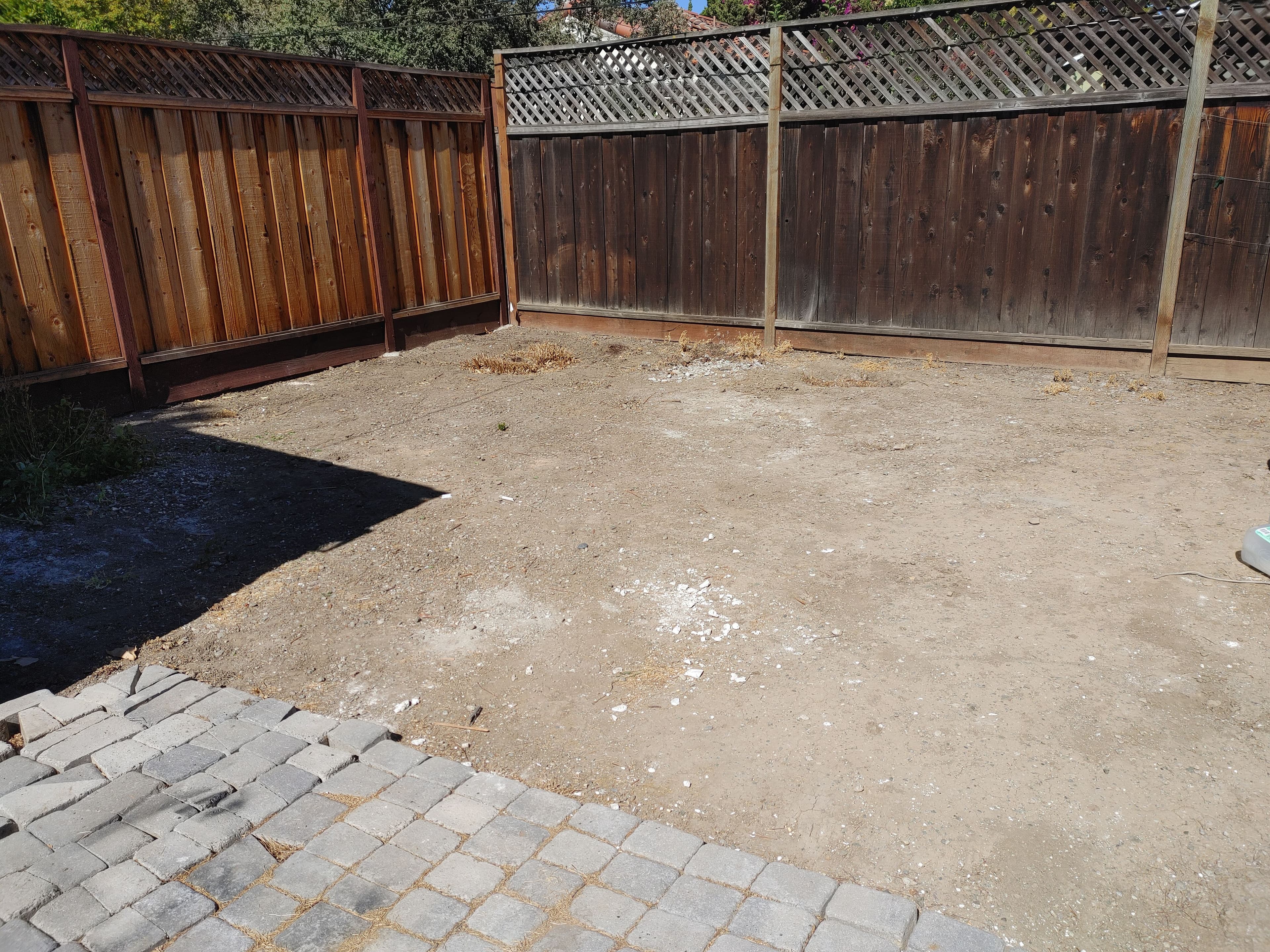 Empty backyard space with dirt and gravel, bordered by wooden fences. Ideal for landscaping projects.