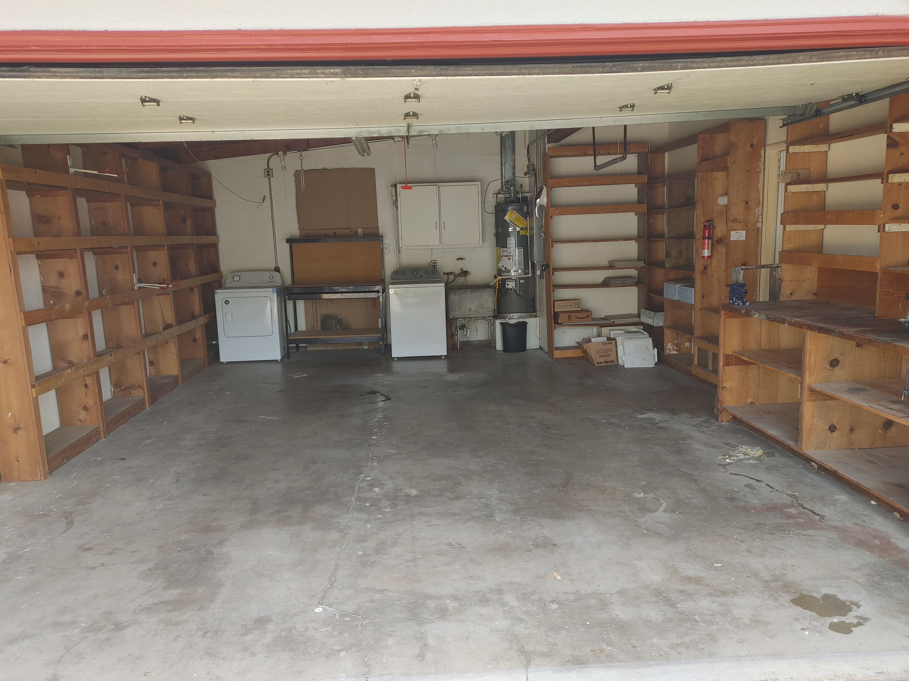 Spacious garage with wooden shelves, washer, dryer, and concrete floor. Ideal for storage.