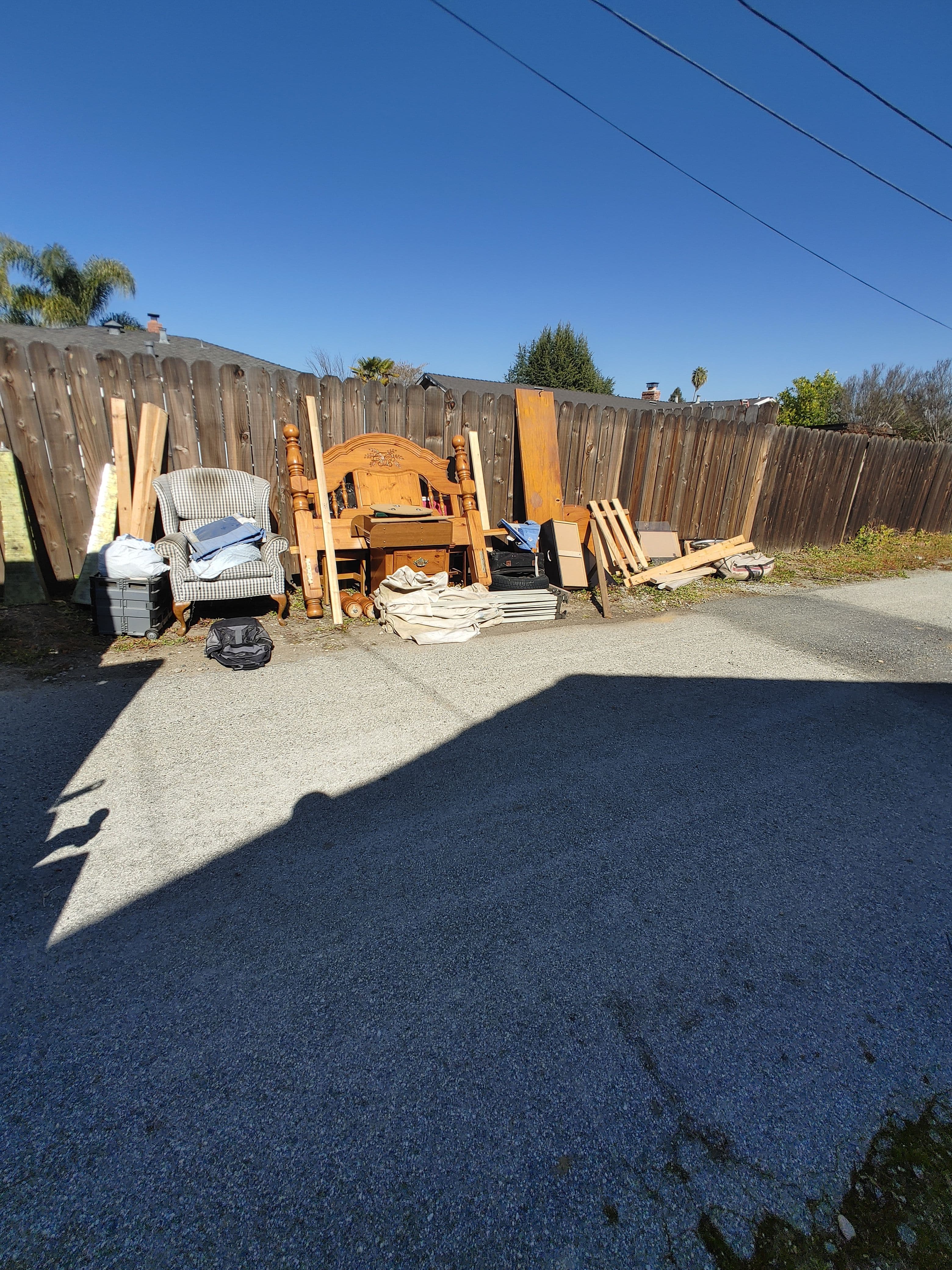 Pile of discarded furniture and materials in an outdoor area with clear blue sky.