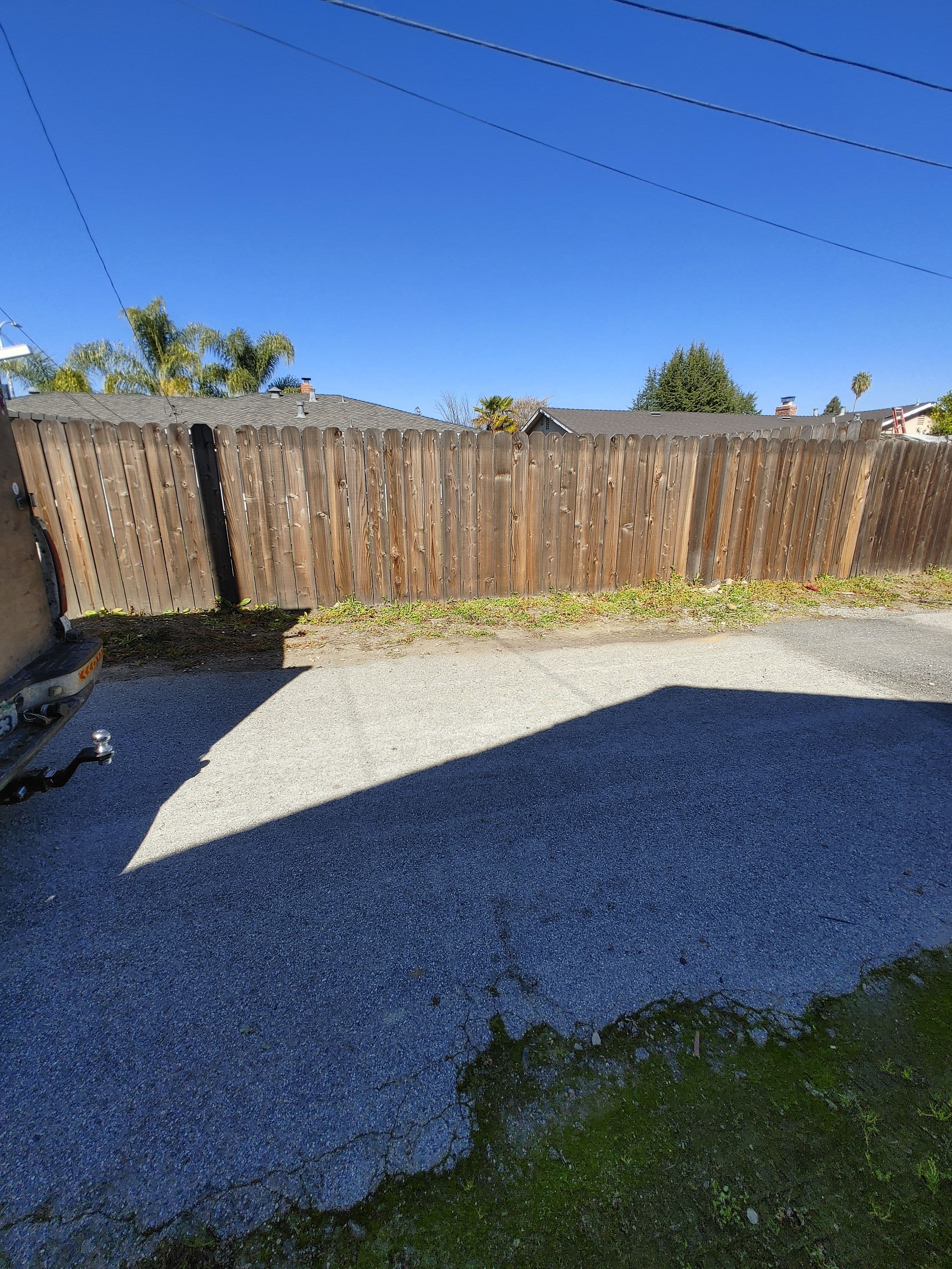 Wooden fence along a gravel path under a clear blue sky in a residential area.