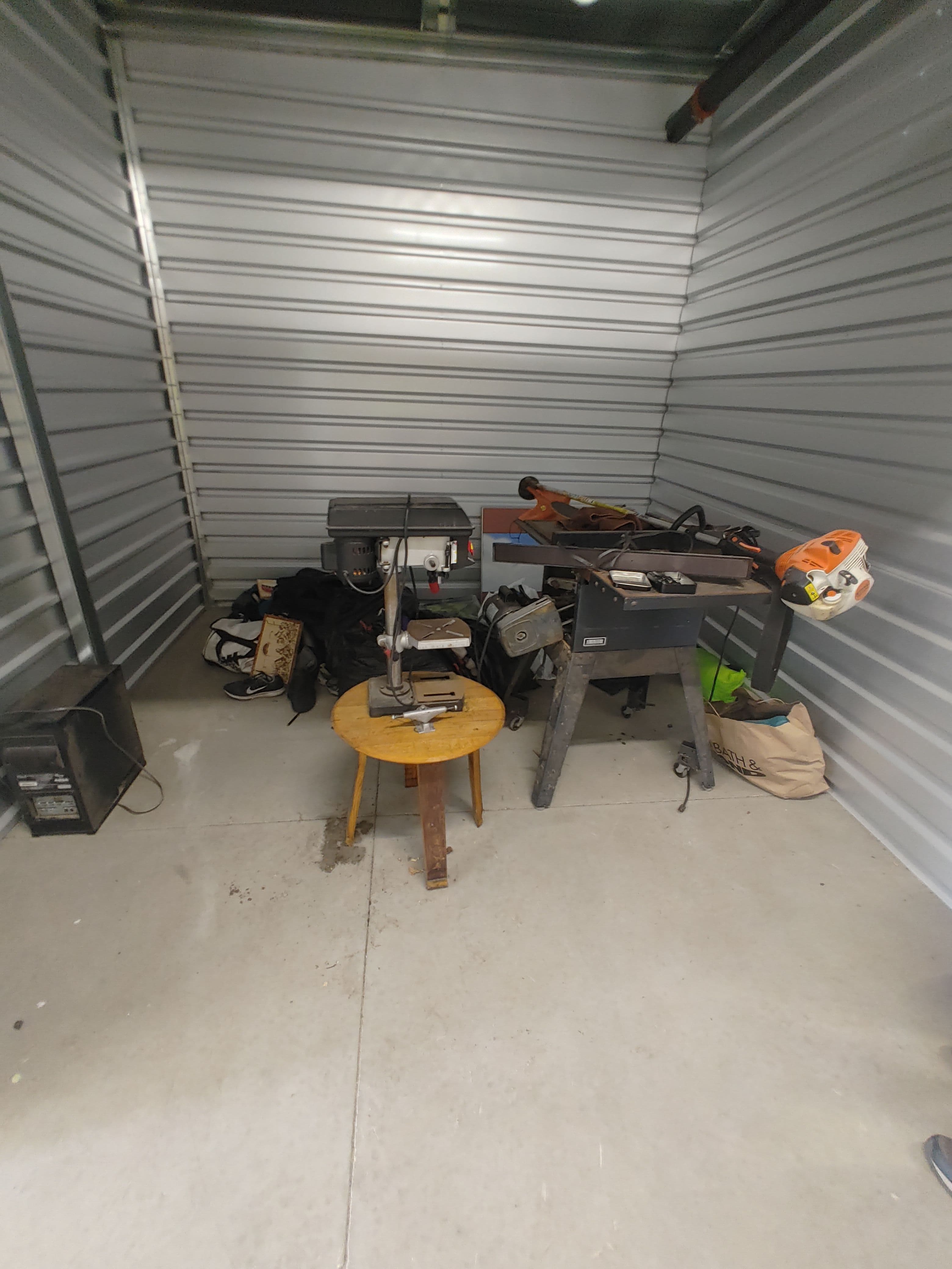 Cluttered storage unit with tools, including a table saw, drill, and assorted equipment.