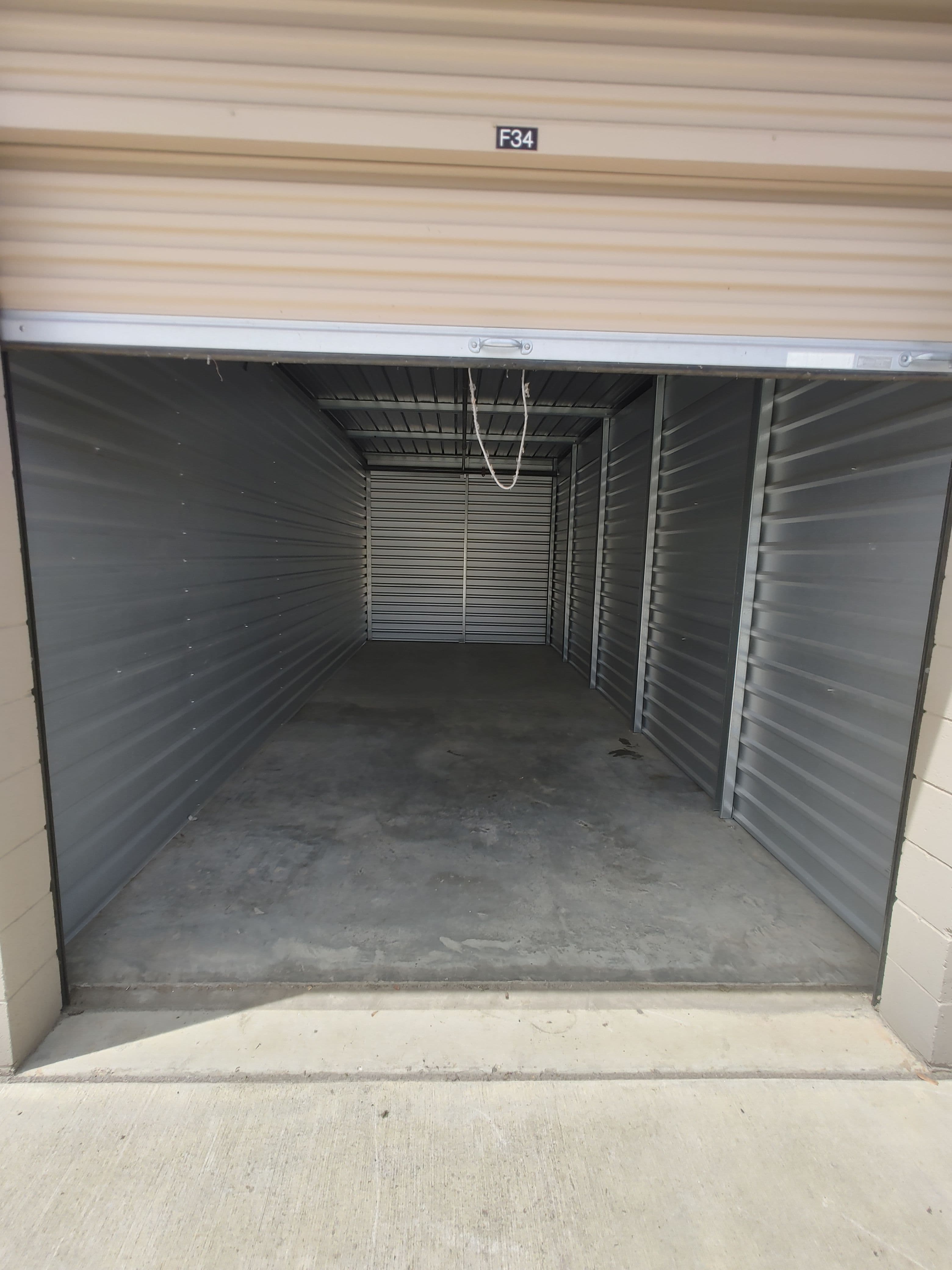Empty storage unit F34 with metallic walls and concrete floor, ideal for storage solutions.