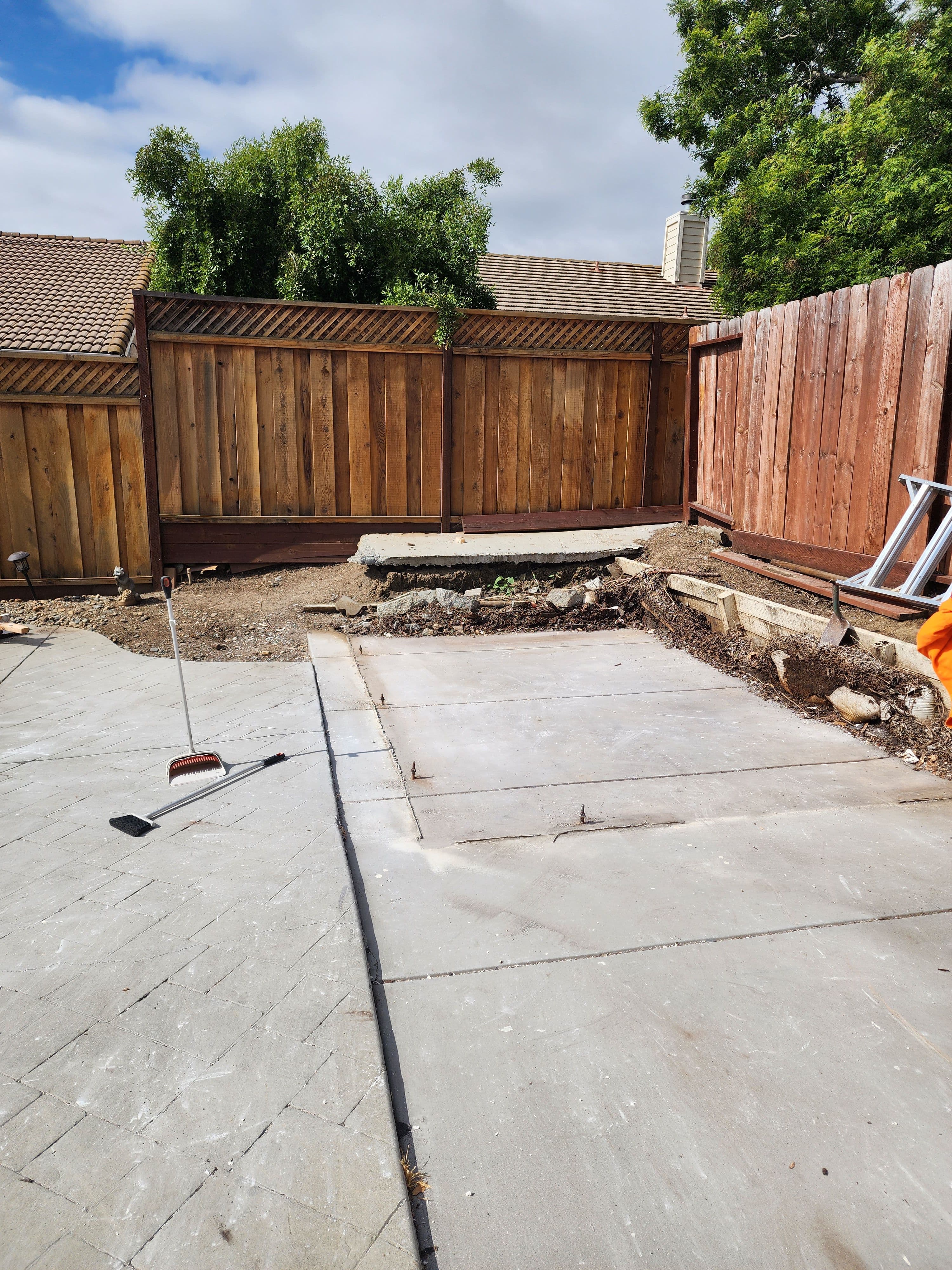 Concrete slab area in a backyard under renovation, surrounded by wooden fences and landscaping.
