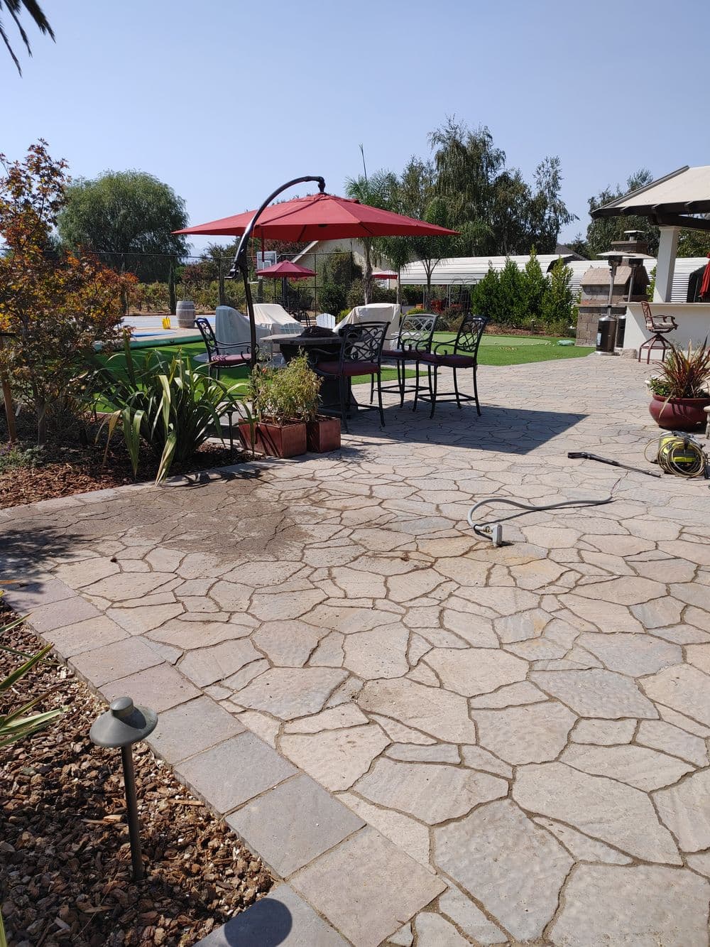 Outdoor patio with stone paving, garden furniture, and a red umbrella in a sunny landscape.