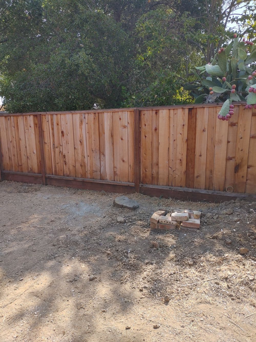 Newly built wooden fence in a yard with soil and construction materials nearby.